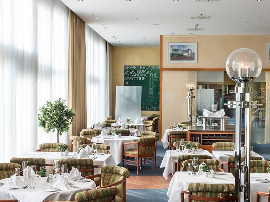 Hotel Restaurant mit weiß eingedeckten Tischen, Weingläsern und Stehlampen 