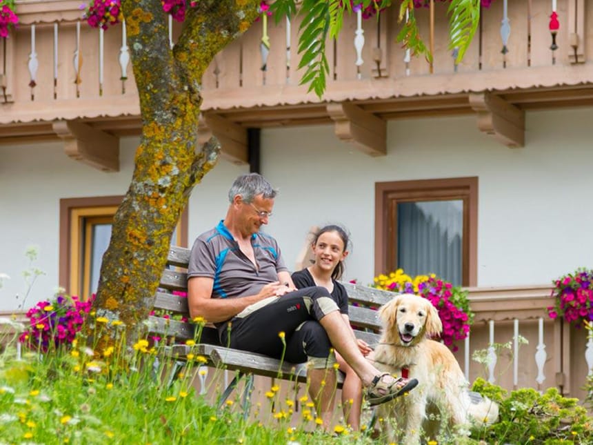 Vater und Tochter mit Hund auf einer Gartenbank