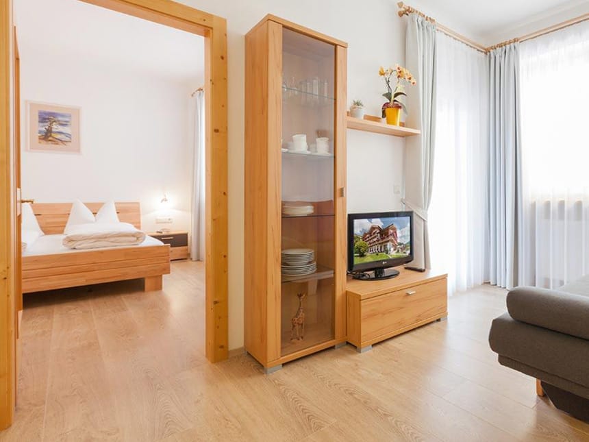 Blick auf Wohn und Schlafraum mit Doppelbett, Vitrine, TV und Couch