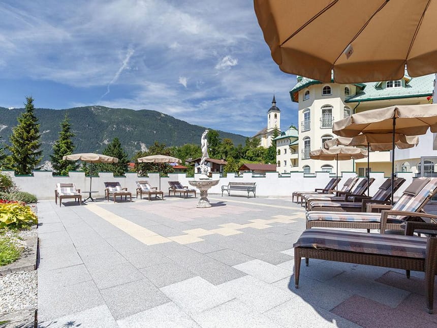 Terrasse bei Sonnenschein mit Relaxliegen und Sonnenschirmen sowei Blick auf die Berge