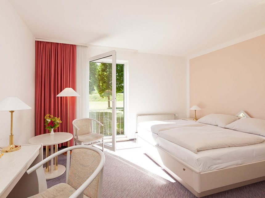 helles Doppelzimmer mit Boxspringbett, Stehlampe, Tisch, tuhl und Balkon